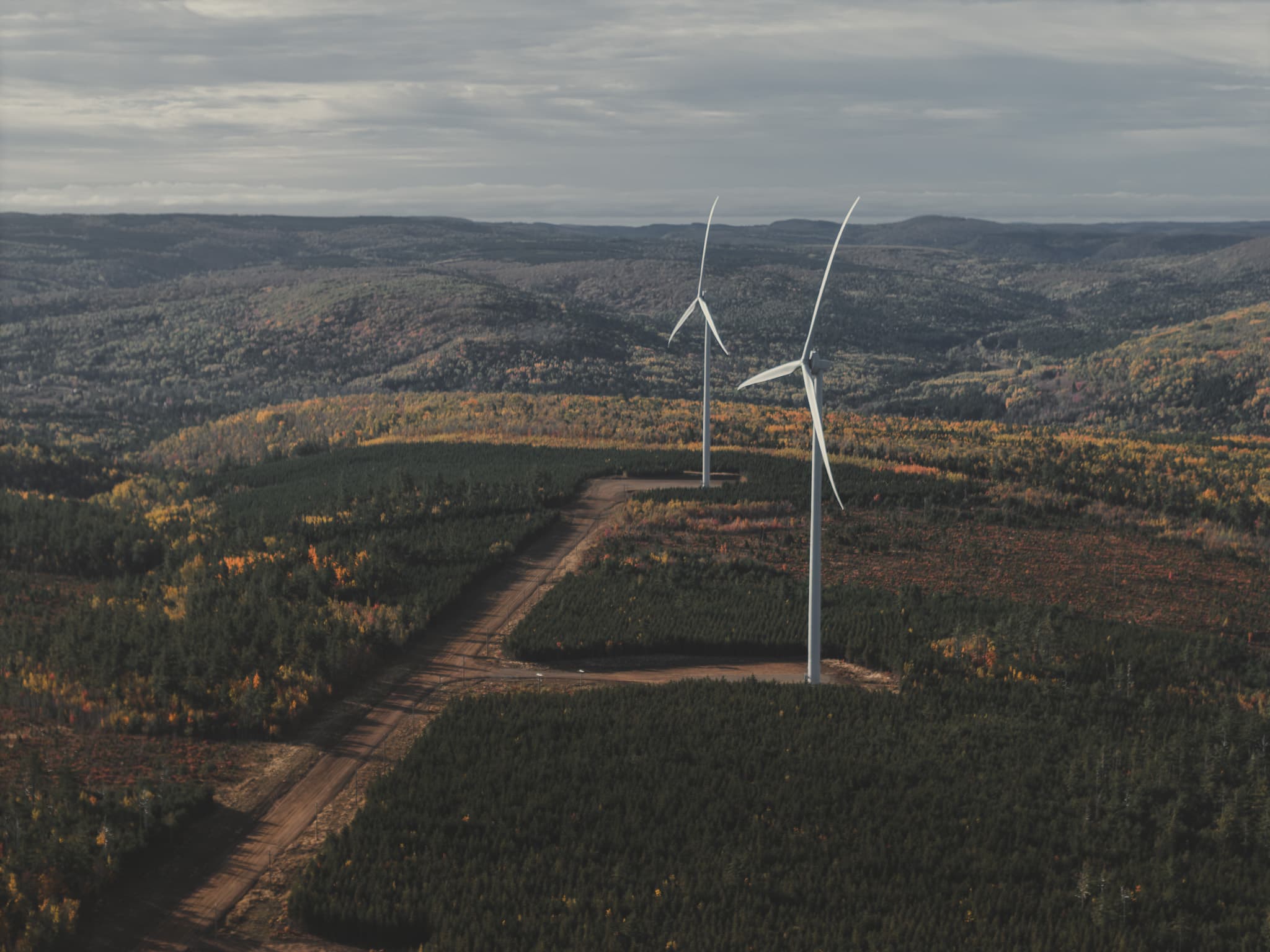 Aerial of two wind turbines over autumn forest hills